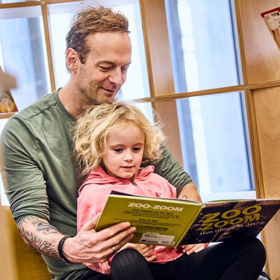 Far og datter på biblioteket læser en bog