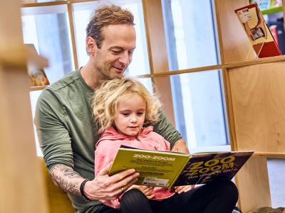 Far og datter på biblioteket læser en bog