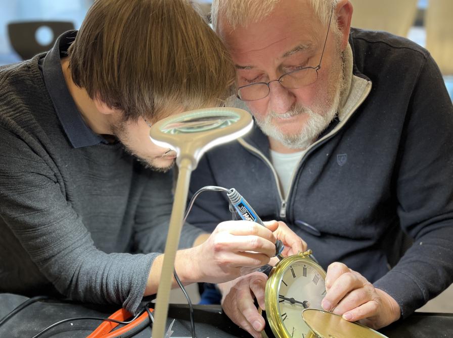 Billede af 2 frivillige i Repair cafeen som er i gang med at reparere et ur