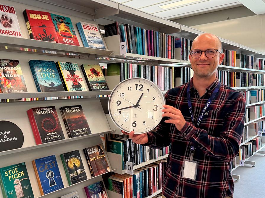Mads Einar Nielsen holder et væg-ur i biblioteksrummet.